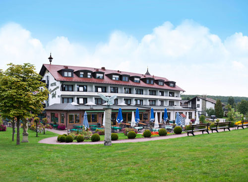 Best Western Hotel Brunnenhof Hotel mit Außensitzbereich, umgeben von Bäumen und Grün unter blauem Himmel.